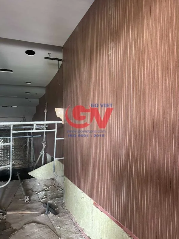Cận cảnh vách ốp vân gỗ có các rãnh dọc đang được lắp đặt trong không gian hội trường.