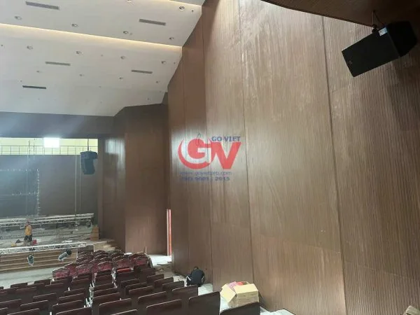 Không gian hội trường với vách ốp vân gỗ màu nâu, trần đèn âm và hàng ghế khán giả.